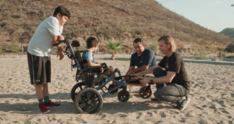 a beach with people inspecting a wheelchair and how it works on sand